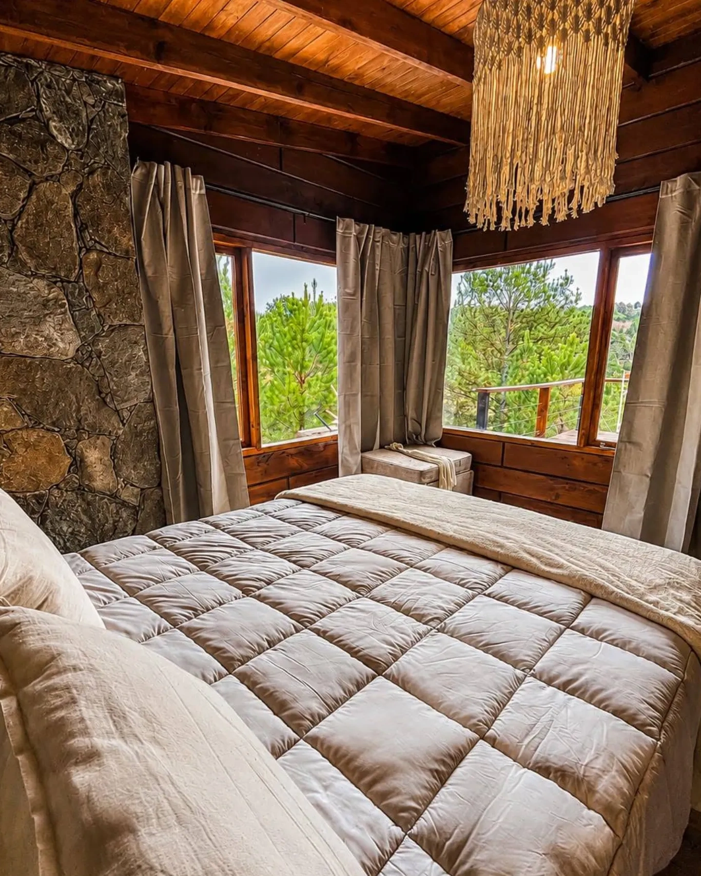 Habitación matrimonial con ventanales al bosque y pared de piedra
